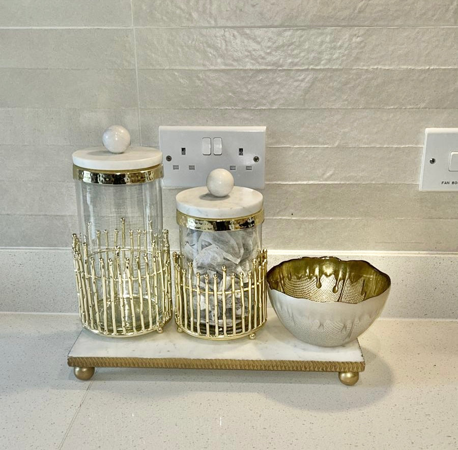 two glass canisters in gold metal base and marble lid on a marble tray kitchen decor