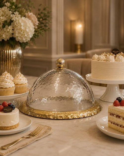 Dessert table with cakes, cupcakes, and a decorative glass cloche.
